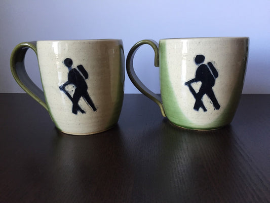 Ceramic coffee mug with  hikers symbol in green and white.