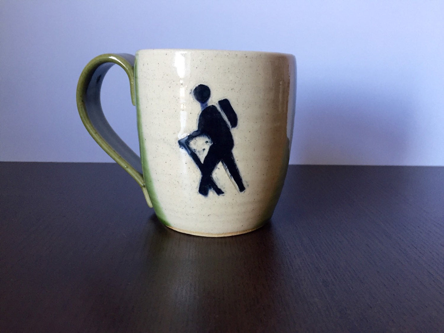 Ceramic coffee mug with  hikers symbol in green and white.
