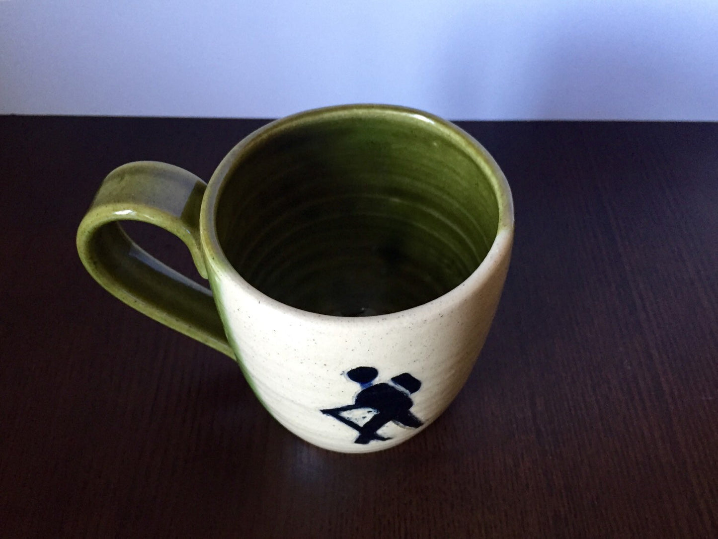 Ceramic coffee mug with  hikers symbol in green and white.